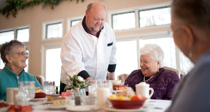 walker methodist chef serving food to residents sitting at a table smiling