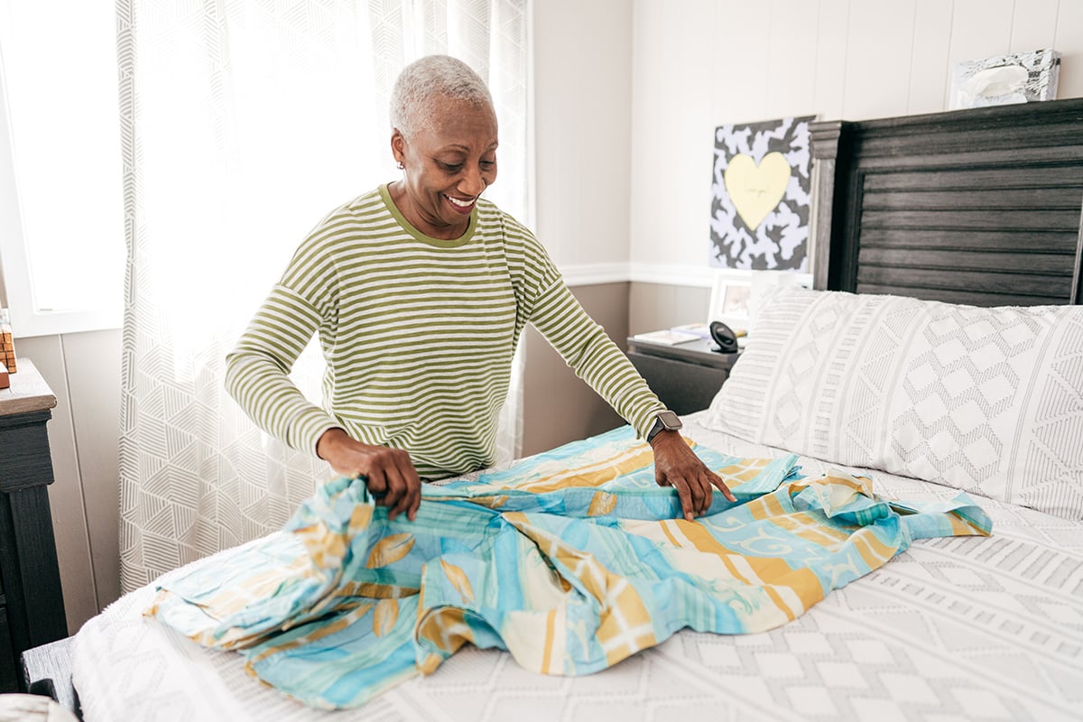 Older woman folds blanket on top of bed