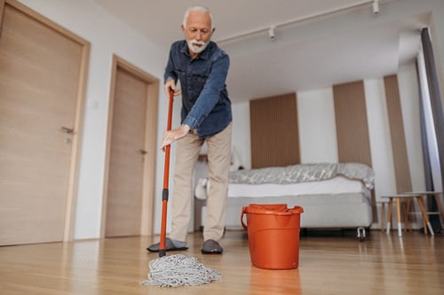 Senior man mops hardwood floors in apartment