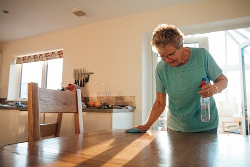 Senior woman with spray bottle wipes down kitchen table