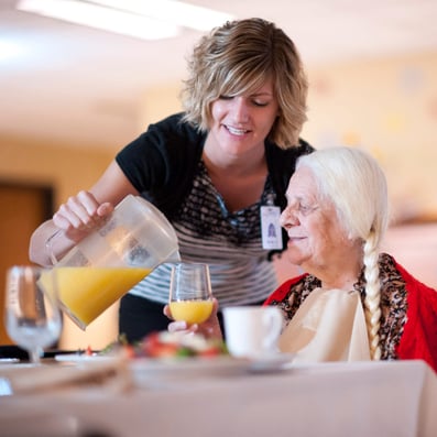 Staff member pours orange juice for senior woman at table