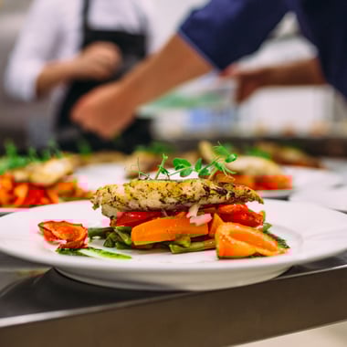 Chicken and vegetables on plate in front of kitchen culinary team