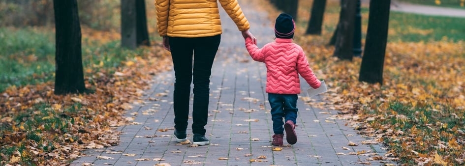 woman holding child's hand walking down the sidewalk